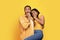 Frightened excited young african american couple, lady biting fists, afraid, isolated on yellow background, studio