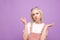 Frightened girl, a teenager with light hair and sweet clothes, stands on a blue background, puzzled looking at the camera and