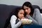 Frightened girls sisters sitting on the sofa looking at the camera. Watching tv horror film together with popcorn