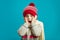 Frightened little girl in red winter hat with pompom and wrapped a scarf, put her hands to cheek, expresses surprise and