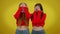 Frightened scared twin sisters closing face with hands shaking head. Portrait of young Caucasian women posing at yellow