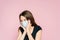 Frightened young woman in a protective mask on a pink background. Fear and horror of the coronavirus pandemic