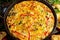 Frittata made of eggs, potato, bacon, paprika, parsley, green peas, onion, cheese in iron pan. on wooden table.