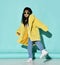 Frolic asian kid girl in stylish yellow furry coat, jeans, sneakers and sunglasses dances stands with her foot up