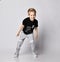 Frolic blond kid boy in sunglasses, black t-shirt with dinosaur print and gray pants stands leaning forwards going to run