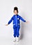 Frolic dark-skinned sporty kid girl in blue jumpsuit stands holding arms spread in ready to jump or landing pose