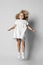 Frolic playful blonde curly kid girl in white casual dress and sneakers is moving, jumping, having fun