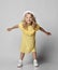 Frolic playful blonde curly kid girl in yellow dress, white hat and sneakers is moving, dancing, jumping, having fun