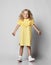 Frolic playful blonde curly kid girl in yellow dress and white sneakers is having fun, funny posing, playing