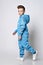 Frolic smiling kid boy in blue jumpsuit with hood and pockets with reflective stripes walks. Side view