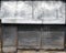 The front of an abandoned store on a street with closed rusting metal shutters over the shop front and door