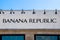 Front of Banana Republic Store with liights above signon rough stucco surface and strip of blue sky in Utica