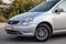 Front bumper and hood view of a Honda Stream car in a silver body Japanese 2002 year van in a parking lot with a green trees and