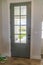 Front door with balck knob and glass panes against white wall and wood floor