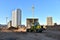 Front-end loader and excavator on road work. Tower crane in action at construction site. Earth-moving heavy equipment for road