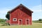 A front facing view of a wonderful old red barn with white trim and landscaped lawn with  dirt road
