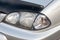 Front headlight view of Toyota Caldina car of 2000 release in the back of a silver T210 station wagon in a parking lot with a