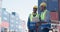 In front of a large industrial harbor with cargo background, two engineer male worker dockers in checking examine discussion with