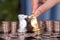 In front of a large number of dollar coins, a hand helps the silver horse chess piece to defeat the golden horse chess piece