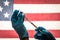 Front Line Worker Holding Syringe and Vial Filled with Coronavirus Vaccine or Medicine Silhouetted Against American Flag