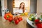 Front low-angle view of young redhead woman cutting fresh lettuce preparing food salad sitting at table in modern