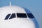 The front nose and cockpit of an Airbus A319-100 passenger plane, the cockpit glazing, blue sky in the background