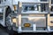 Front part of white big rig semi truck with powerful aluminum grille guard and headlight assembly