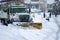 Front right view of city services snowplow truck clearing roadways of snow after winter storm covered streets in urban area