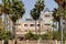 Front shot of Ciutat Jardi hotel with tall palm trees before it and a parking sign