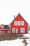 A front shot of a red wooden house with several white windows with a tube coming through a dark roof. Clear white sky is on top of