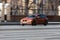 Front side view of BMW 1 Series in motion. Orange hatchback car moving on the street