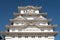 Front symmetrical view of white Himeji Castle tower, with traditional carved roof and blue sky background, Himeji, Japan.