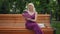 Front view adult woman reading out loud smiling sitting on bench in summer park. Portrait confident smart Caucasian lady