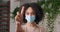 Front view afro american masked woman standing alone isolated during pandemic holding palm in front of her calling keep