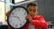 Front view of Asian schoolboy holding wall clock at desk in classroom at school 4k