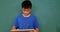 Front view of Asian schoolboy writing and showing text on slate chalkboard in classroom at school 4k