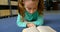 Front view of attentive Caucasian schoolgirl reading a book in library at school 4k