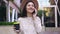 Front view of attractive elated young lady in lovely hat with her fresh coffee in hand talking on phone while going near