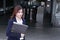 Front view of attractive young Asian business woman with ring binder walking up the stairs at entrance of railway station backgrou