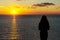 Front view of a back light of faithful woman silhouette holding sun on the beach at sunrise with a warm background