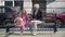 Front view beautiful granny and girl sitting on bench on city street talking as girl running away with balloon. Wide