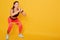Front view of beautiful slim muscular female with resistance band performing squats isolated over yellow background, sporty woman