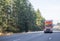 Front view of big rig orange semi truck with semi trailer driving up the hill on wide multiline highway