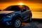 Front view blue compact SUV car with sport and modern design parked on concrete road by the sea at sunset. Electric car technology