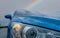 Front view of blue luxury SUV car parked near sea beach on rainy day with rainbow as background. Raindrops on blue texture of car