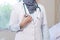 Front view body part of hijab female doctor hand holding stethoscope head inside a hospital room using white lab coat and grey sca