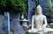 Front view of a Buddha statue with blue grey rocks in the background and bamboo trees. Enlightment concept