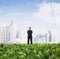 Front view of businessman with arms crossed standing in a green field with city skyline in the background