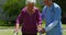 Front view of Caucasian female doctor helping senior patient to walk with walker in the garden of nu