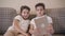 Front view close-up of two Caucasian twin brothers looking at tablet screen and smiling. Siblings resting on the